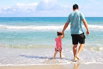 man holding child's hand on beach